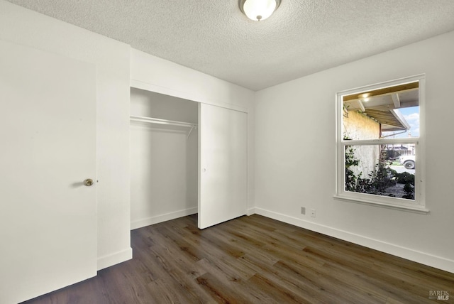 unfurnished bedroom featuring a closet, dark wood finished floors, a textured ceiling, and baseboards