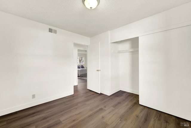 unfurnished bedroom with a closet, visible vents, a textured ceiling, wood finished floors, and baseboards