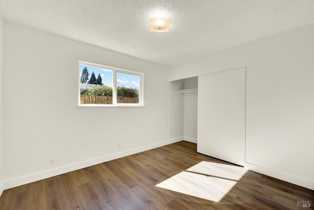 unfurnished bedroom with a textured ceiling, a closet, wood finished floors, and baseboards