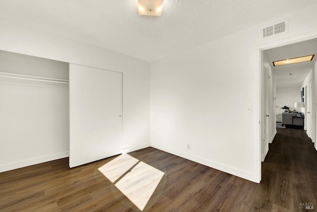 unfurnished bedroom featuring baseboards, visible vents, dark wood-type flooring, a textured ceiling, and a closet