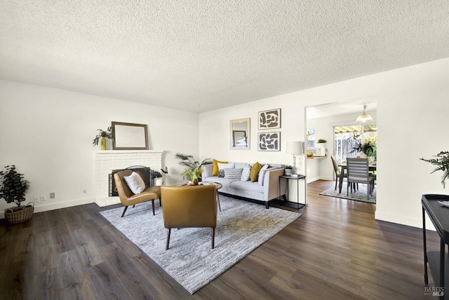 living area featuring a brick fireplace, a textured ceiling, baseboards, and dark wood-type flooring