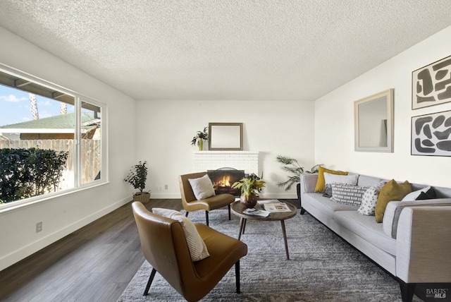 living area with a fireplace, a textured ceiling, baseboards, and wood finished floors