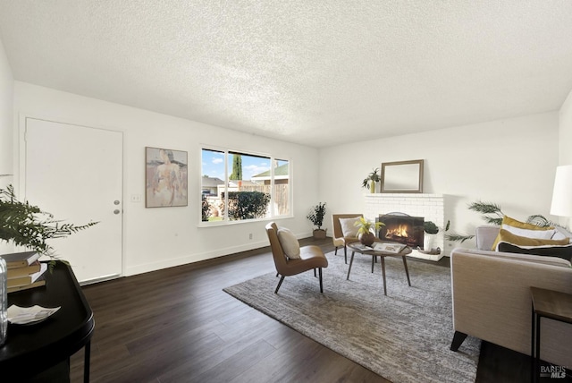 living room featuring a brick fireplace, a textured ceiling, baseboards, and dark wood-type flooring