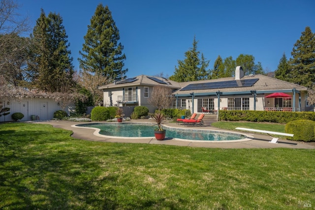 rear view of property featuring an outdoor pool, a yard, a chimney, and solar panels