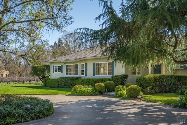 view of front of home with concrete driveway, a front lawn, a tile roof, and stucco siding