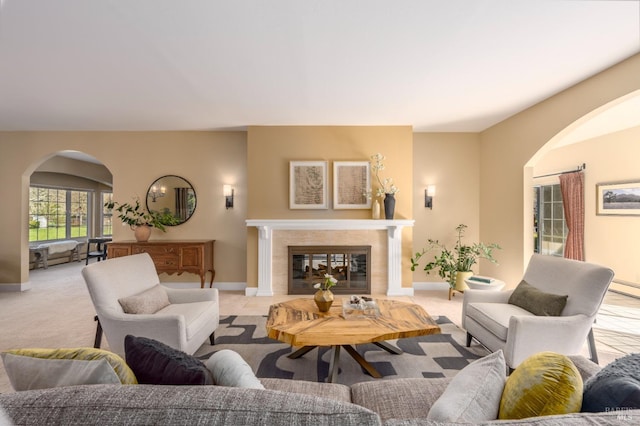 living room with arched walkways, carpet floors, a tile fireplace, and baseboards