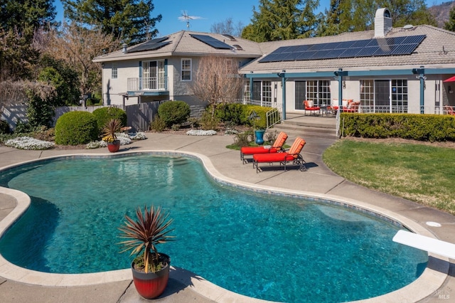 rear view of property with an outdoor pool, a tile roof, roof mounted solar panels, a chimney, and a patio area