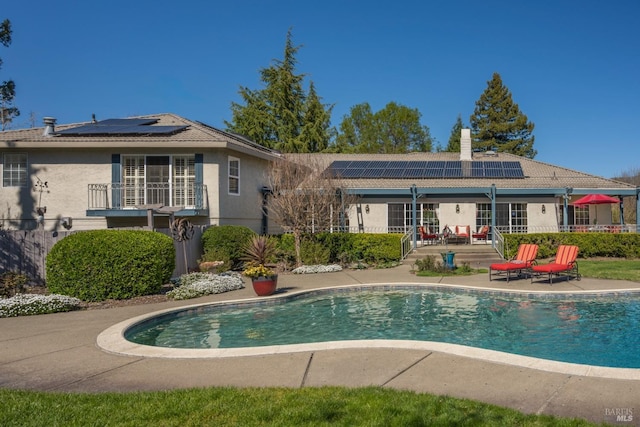 rear view of property featuring roof mounted solar panels, a patio area, an outdoor pool, and stucco siding