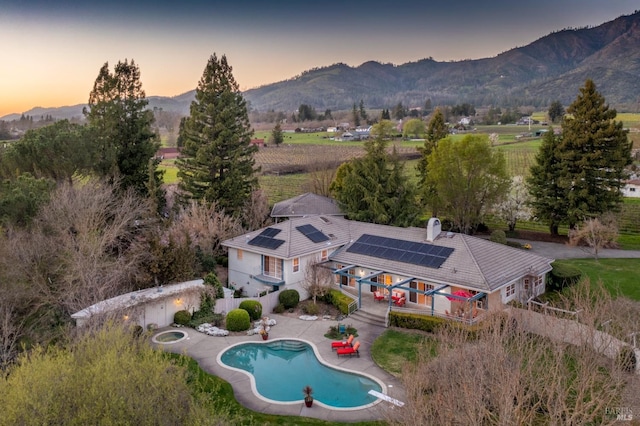 exterior space featuring a patio, a mountain view, roof mounted solar panels, an outdoor pool, and a chimney