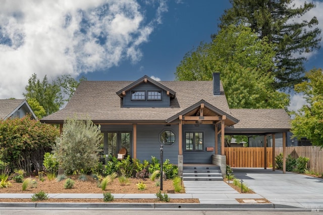 view of front facade featuring roof with shingles, covered porch, fence, a carport, and driveway