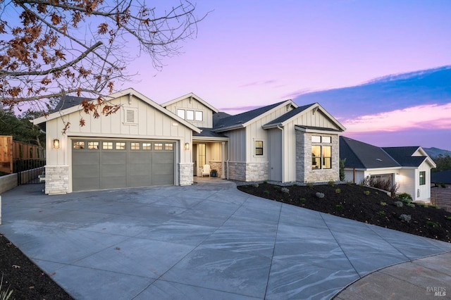 modern farmhouse style home with board and batten siding, fence, a garage, stone siding, and driveway