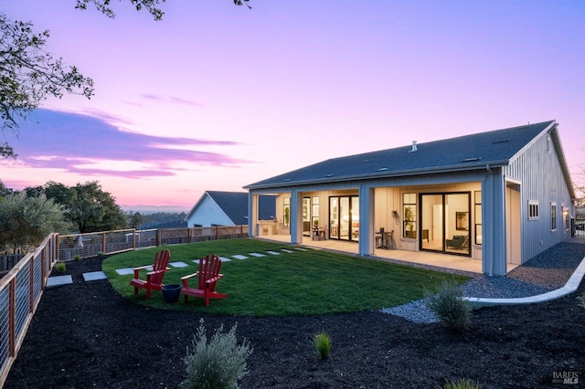 back of house featuring board and batten siding, a patio area, a fenced backyard, and a lawn