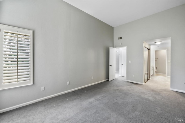 unfurnished bedroom featuring visible vents, baseboards, ensuite bath, a high ceiling, and carpet flooring