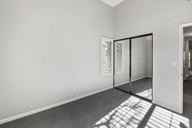 unfurnished bedroom featuring carpet floors, a high ceiling, a closet, and baseboards