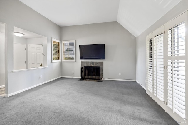 unfurnished living room with vaulted ceiling, dark colored carpet, a tiled fireplace, and baseboards