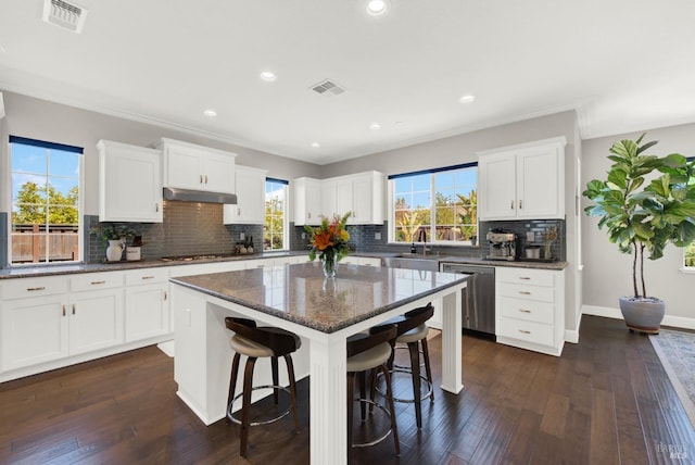 kitchen featuring visible vents, dishwasher, dark wood-style floors, a kitchen island, and a breakfast bar area