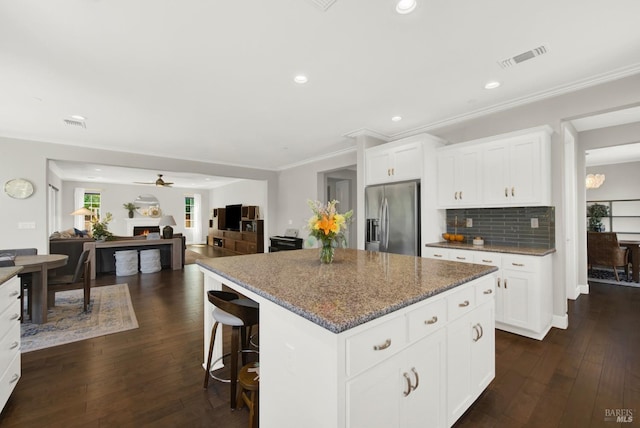 kitchen featuring stainless steel fridge, dark stone countertops, a center island, dark wood-style flooring, and a lit fireplace