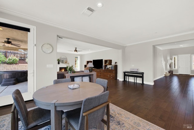 dining space with a lit fireplace, dark wood finished floors, visible vents, and crown molding