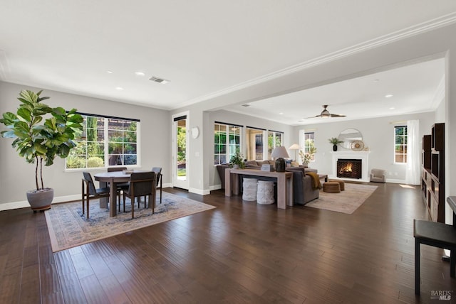 dining room featuring dark wood-style flooring, crown molding, visible vents, a warm lit fireplace, and baseboards