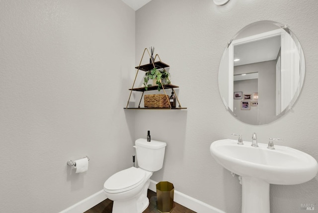 half bath featuring wood finished floors, toilet, and baseboards