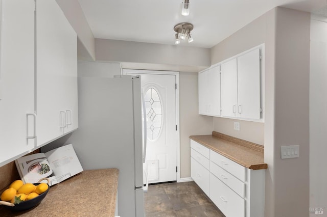 kitchen featuring light countertops, freestanding refrigerator, and white cabinets