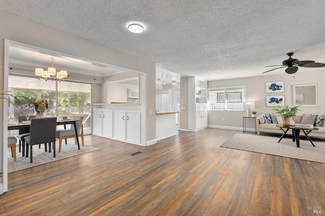 interior space with a textured ceiling, ceiling fan with notable chandelier, visible vents, baseboards, and wood-type flooring