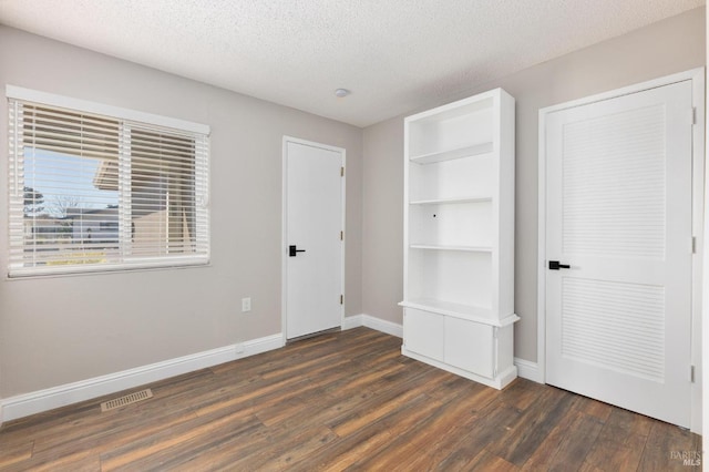 unfurnished bedroom with a textured ceiling, dark wood finished floors, visible vents, and baseboards