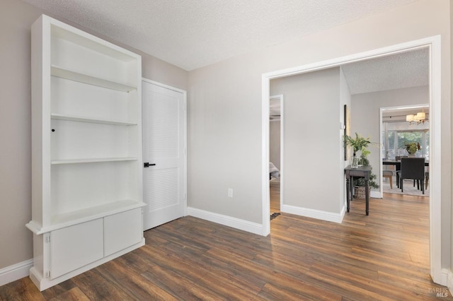 unfurnished bedroom featuring dark wood-type flooring, a textured ceiling, baseboards, and an inviting chandelier