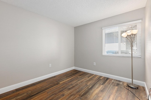 spare room featuring a textured ceiling, dark wood-type flooring, visible vents, and baseboards