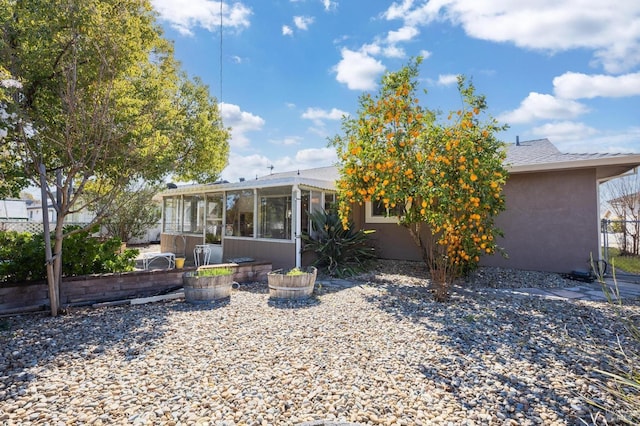 rear view of property with a sunroom, roof with shingles, fence, and stucco siding