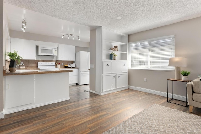 kitchen featuring white appliances, white cabinets, wood finished floors, a peninsula, and a textured ceiling