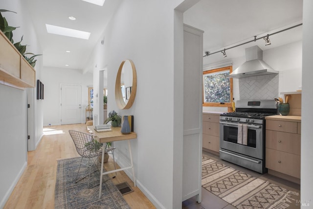 kitchen with a skylight, tasteful backsplash, light wood-style flooring, stainless steel gas stove, and wall chimney range hood