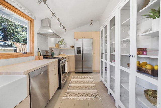 kitchen featuring stainless steel appliances, light countertops, wall chimney range hood, light brown cabinets, and light tile patterned flooring