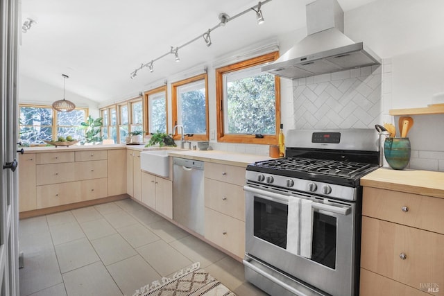 kitchen featuring stainless steel appliances, light countertops, wall chimney range hood, and light brown cabinetry