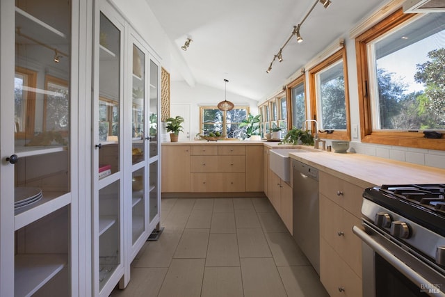 kitchen with a sink, vaulted ceiling, appliances with stainless steel finishes, light brown cabinetry, and tasteful backsplash