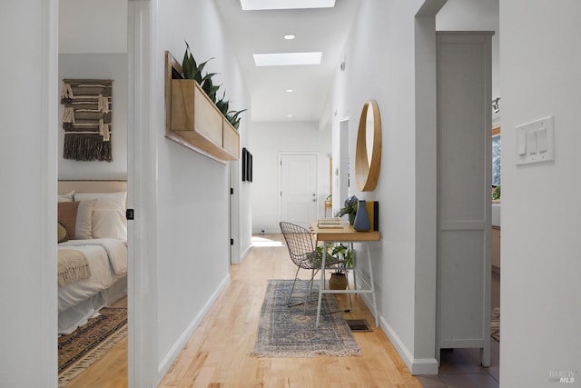 hallway featuring a skylight, light wood finished floors, visible vents, baseboards, and recessed lighting