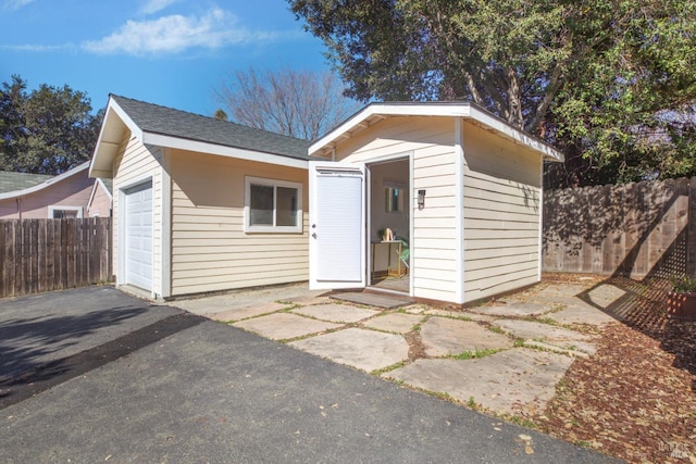 view of front facade with aphalt driveway, an outdoor structure, fence, and a garage