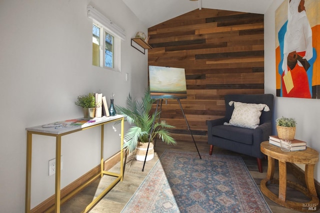 living area featuring an accent wall, vaulted ceiling, wood walls, and wood finished floors