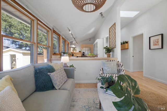 living room with rail lighting, vaulted ceiling with skylight, baseboards, and wood finished floors