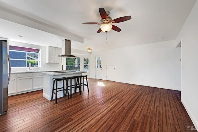 kitchen featuring island exhaust hood, dark wood-style flooring, white cabinets, freestanding refrigerator, and a kitchen bar