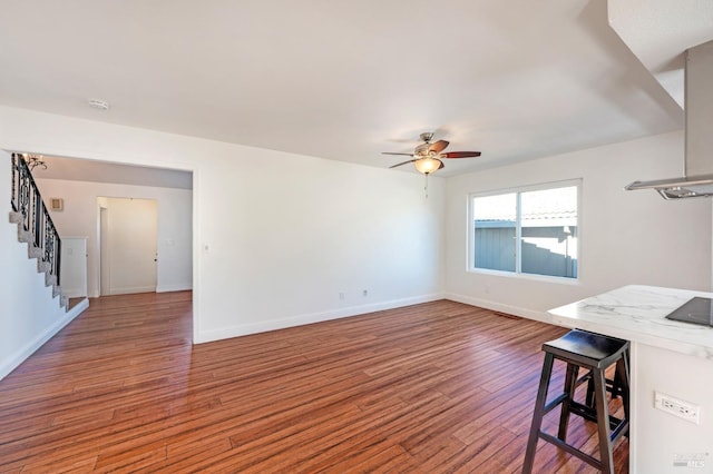 unfurnished living room featuring a ceiling fan, stairs, baseboards, and wood finished floors