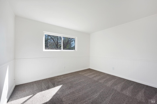 unfurnished room with dark colored carpet and a wainscoted wall