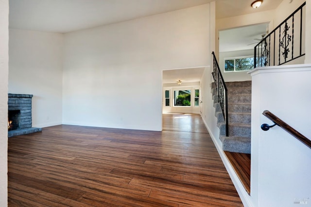 unfurnished living room with baseboards, dark wood-type flooring, a high ceiling, stairs, and a fireplace