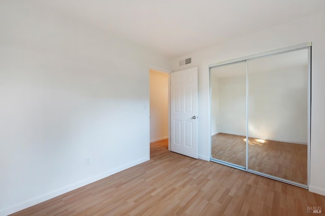 unfurnished bedroom with baseboards, a closet, visible vents, and wood finished floors