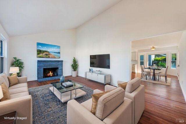 living area featuring a warm lit fireplace, baseboards, high vaulted ceiling, and wood finished floors