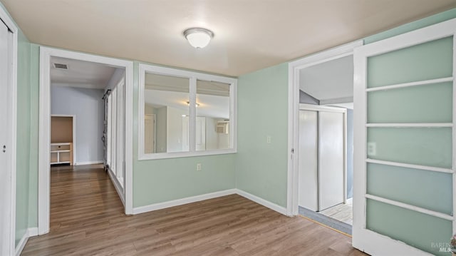 interior space with visible vents, a wall mounted air conditioner, baseboards, and wood finished floors