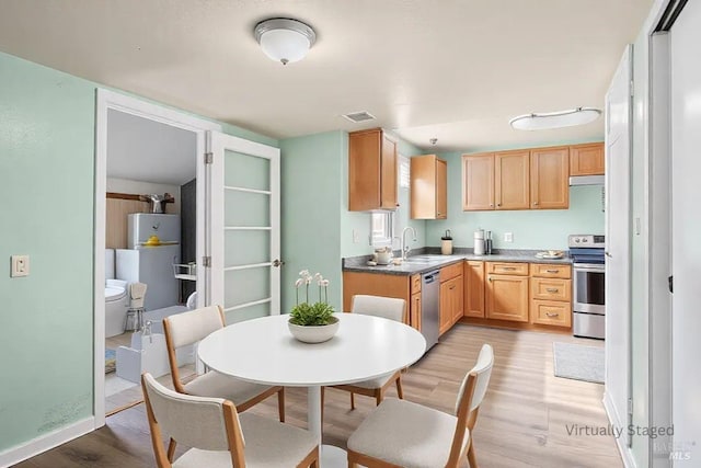 kitchen with visible vents, water heater, light wood-style flooring, stainless steel appliances, and a sink