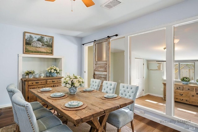 dining area with a ceiling fan, wood finished floors, visible vents, baseboards, and a barn door