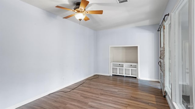 unfurnished room featuring a barn door, baseboards, wood finished floors, and a ceiling fan