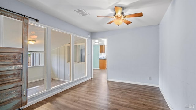 unfurnished room featuring baseboards, wood finished floors, visible vents, and ceiling fan